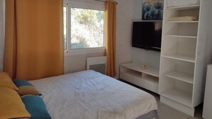 Quarto com cama, televisão na parede, guarda-roupa e janela com cortinas.