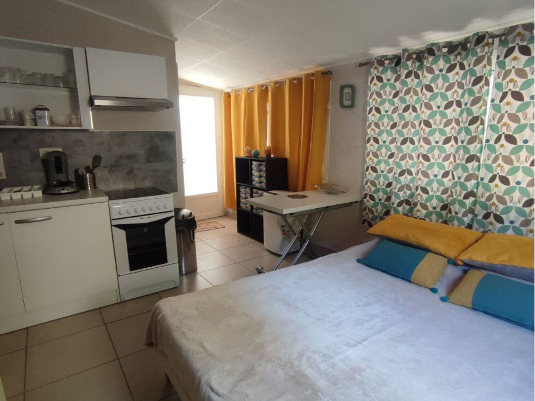 Une pièce de taille modeste comprenant un lit, une kitchenette et une petite table.