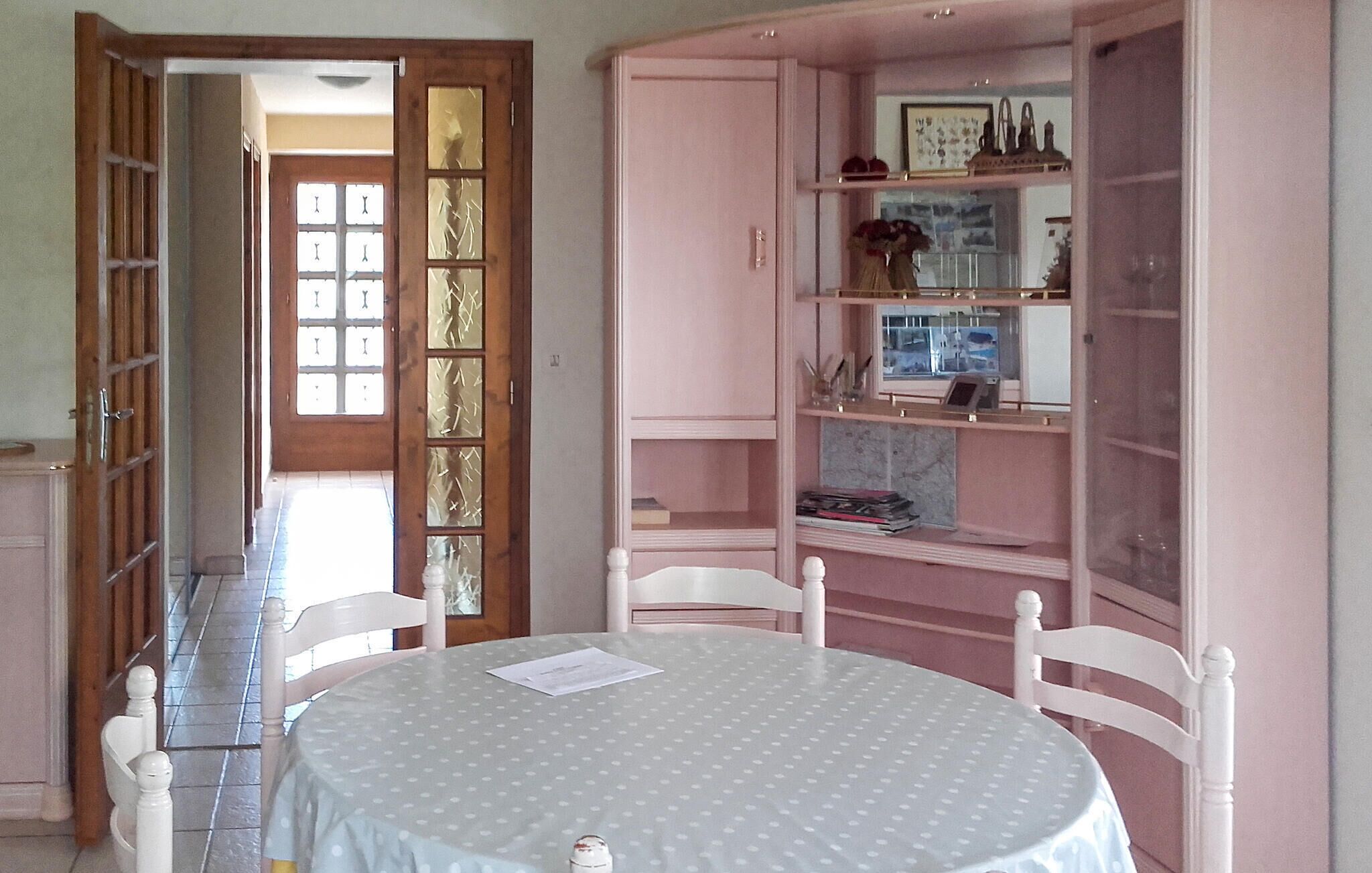 A dining area with a round table, chairs, and a pink cabinet with shelves.