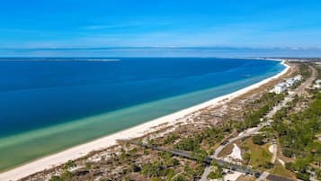 Luchtbeeld van een kustgebied met een strand, een weg en verspreide gebouwen.