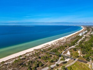An aerial view of a coastal area with a beach, a road, and scattered buildings. - 4 BR Beach House | Golf Cart + Hot Tub + Fire Pit (Port St. Joe)