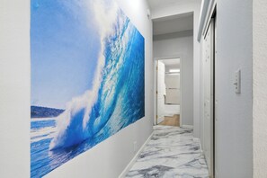 Un couloir orné d’une grande fresque représentant une vague, doté d’un sol en marbre et d’une porte donnant sur une autre pièce.