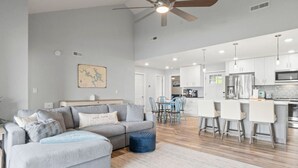 Ein geräumiges Wohnzimmer mit grauem Sofa, einem Essbereich und einer Küche mit weißen Schränken und Edelstahlgeräten.