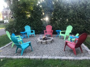 Et bålsted omgivet af farverige Adirondack-stole i et område med grus.