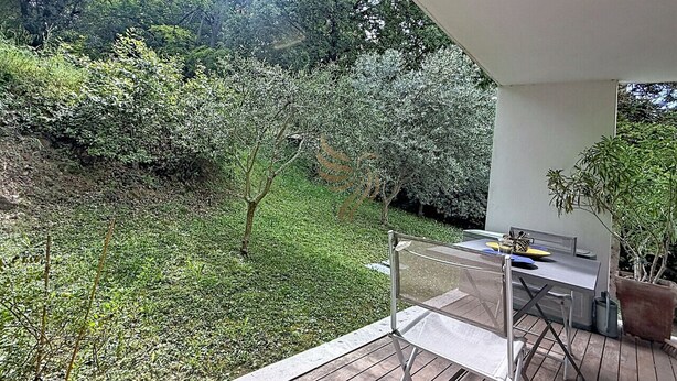 Une terrasse avec une table et des chaises, entourée de verdure et d’arbres.