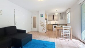 Un espace de vie compact comprenant un canapé, une table à manger avec des chaises, un coin cuisine et une grande fenêtre.