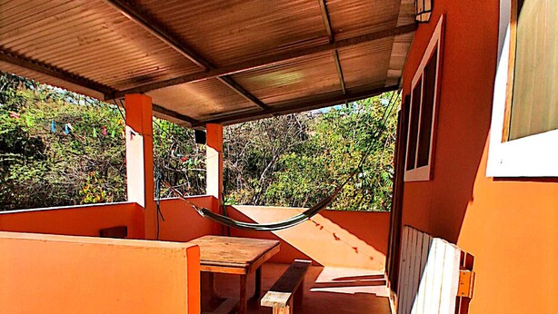 An outdoor patio area with a table and benches, surrounded by orange walls and a metal roof. - New room aere and casita wifi pedasi/venao panama (El Ciruelo)