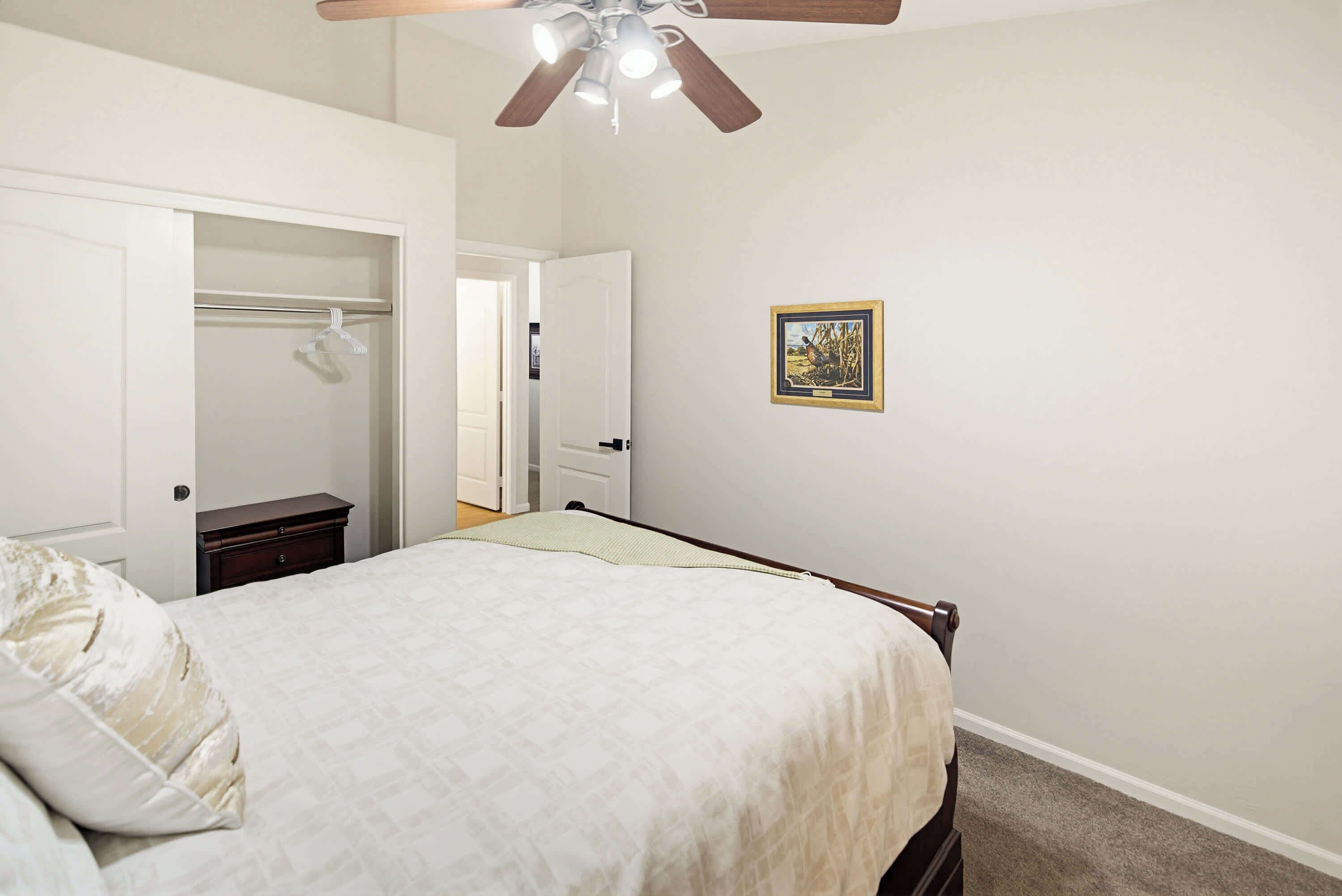 A bedroom with a bed, a closet, a nightstand, a ceiling fan, and a framed picture on the wall.