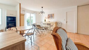 A dining area with a table and chairs, a sofa, a chandelier, and a view of the outdoors. - Charmante maison proche plage (Saint-Georges-d'Oléron)