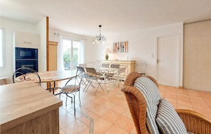 A dining area with a table and chairs, a sofa, a chandelier, and a view of the outdoors. - Charmante maison proche plage (Saint-Georges-d'Oléron)