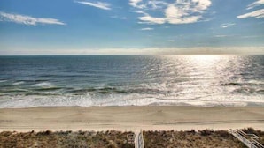 Een strand met heldere lucht, golven en een pad dat naar het water leidt.