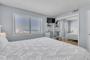 Ein Schlafzimmer mit einem großen Bett, einem Schreibtisch mit Computer, einem Stuhl und einem Fenster mit Jalousien.