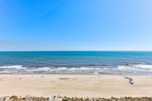 Ein Strand mit blauem Himmel, sandigem Ufer und einigen Personen.
