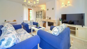 Ein Wohnzimmer mit blauen Sofas, einem Fernseher, einem Schrank und einer Chandelieber.