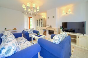 Ein Wohnzimmer mit blauen Sofas, einem Fernseher, einem Schrank und einer Chandelieber.