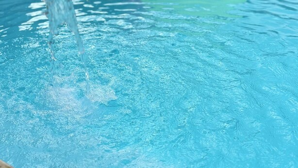 Una piscina con agua entrando, un flotador de flamenco rosa y un flotador circular verde.