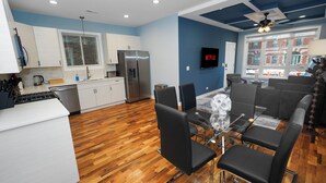 A modern kitchen with a refrigerator, stove, and white cabinets. There is a dining area with black chairs and a glass table. A TV is mounted on the wall, and a window provides a view of the outside. - Urban Chicago 3BR Retreat, 5 min to West Loop (Chicago)