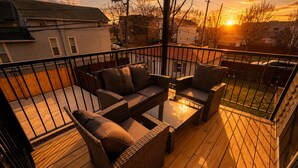 A deck with wicker furniture and a glass table, overlooking a residential area during sunset. - Urban Chicago 3BR Retreat, 5 min to West Loop (Chicago)