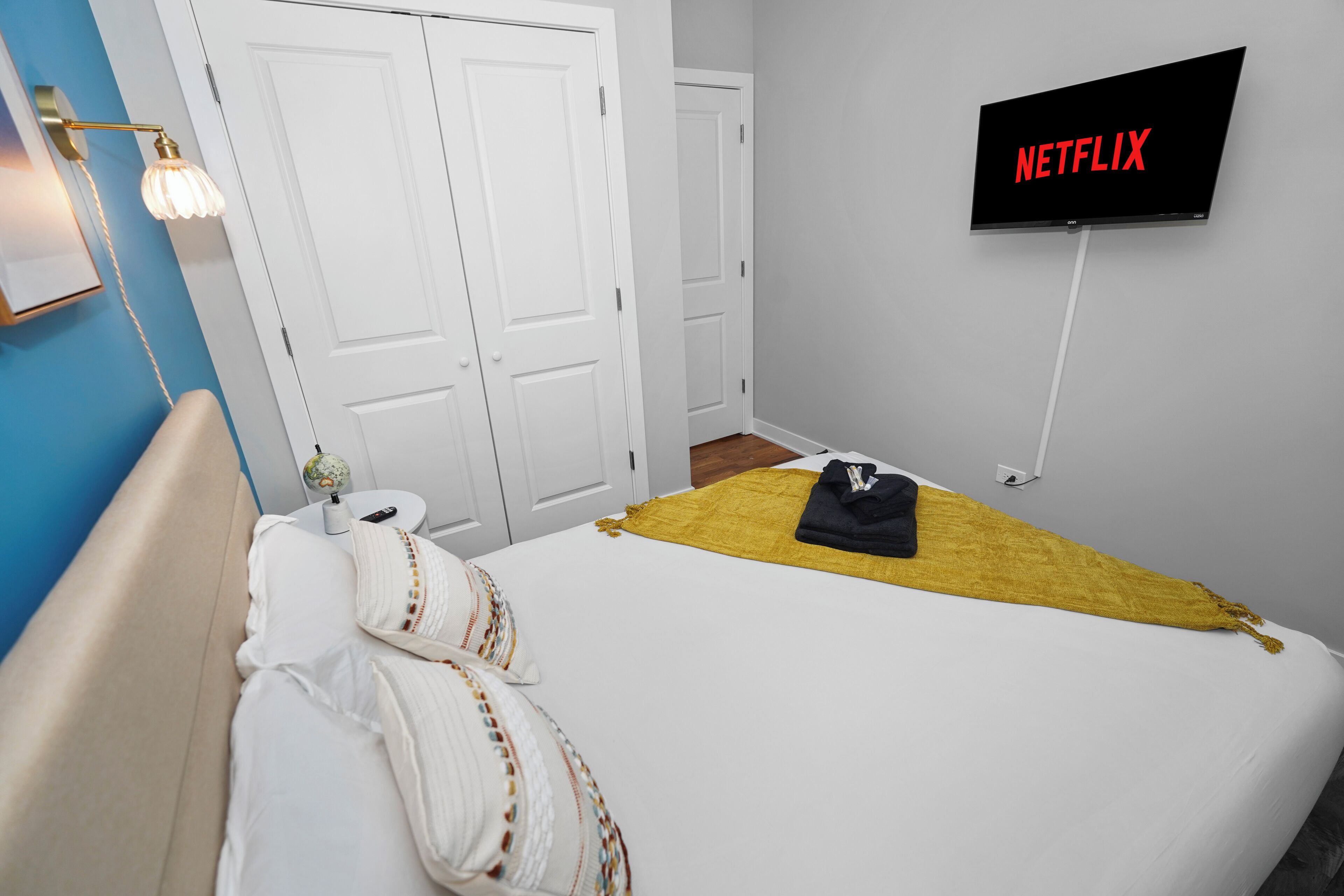 Een hotelkamer met een bed, een televisie waarop 'NETFLIX' staat, een witte deur en een wereldbol op een tafeltje.