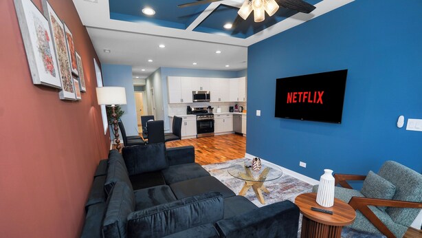 A modern living room with a black sofa, a glass coffee table, and a TV mounted on the wall. - Urban Chicago 3BR Retreat, 5 min to West Loop (Chicago)