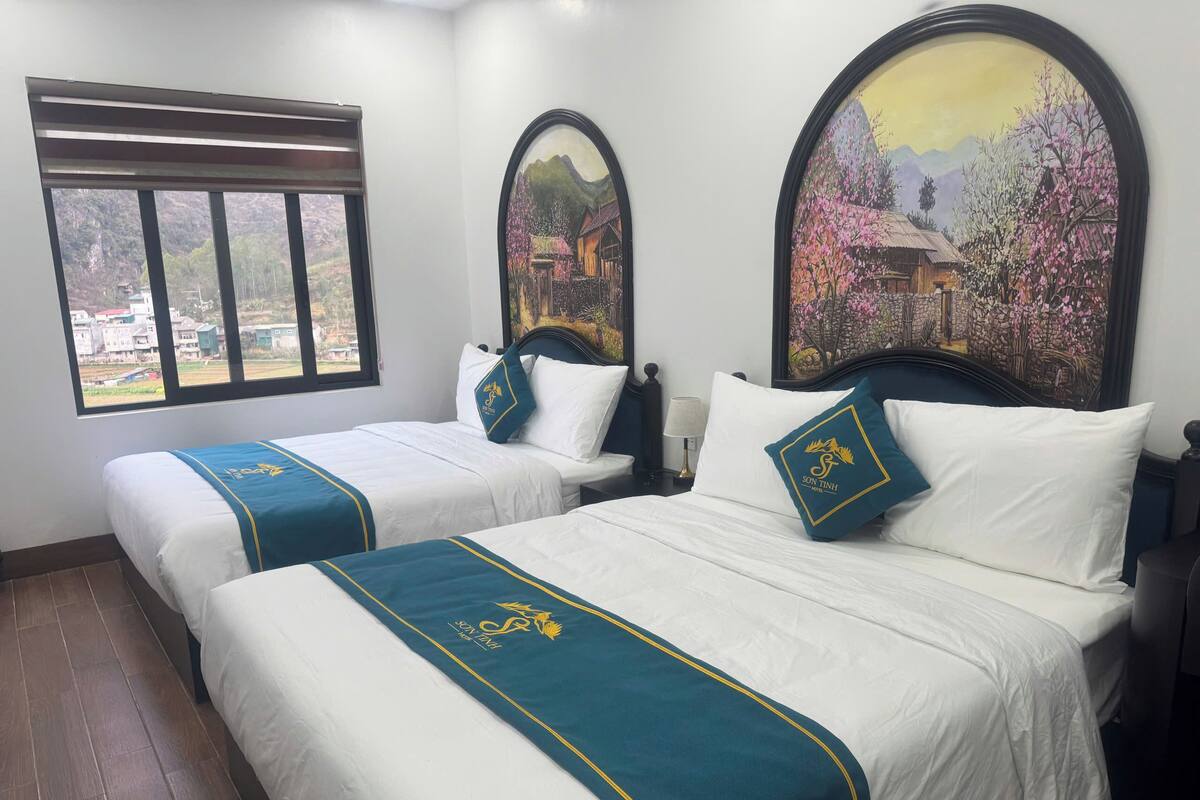 A hotel room with two beds, a window with a view, and two paintings on the wall.