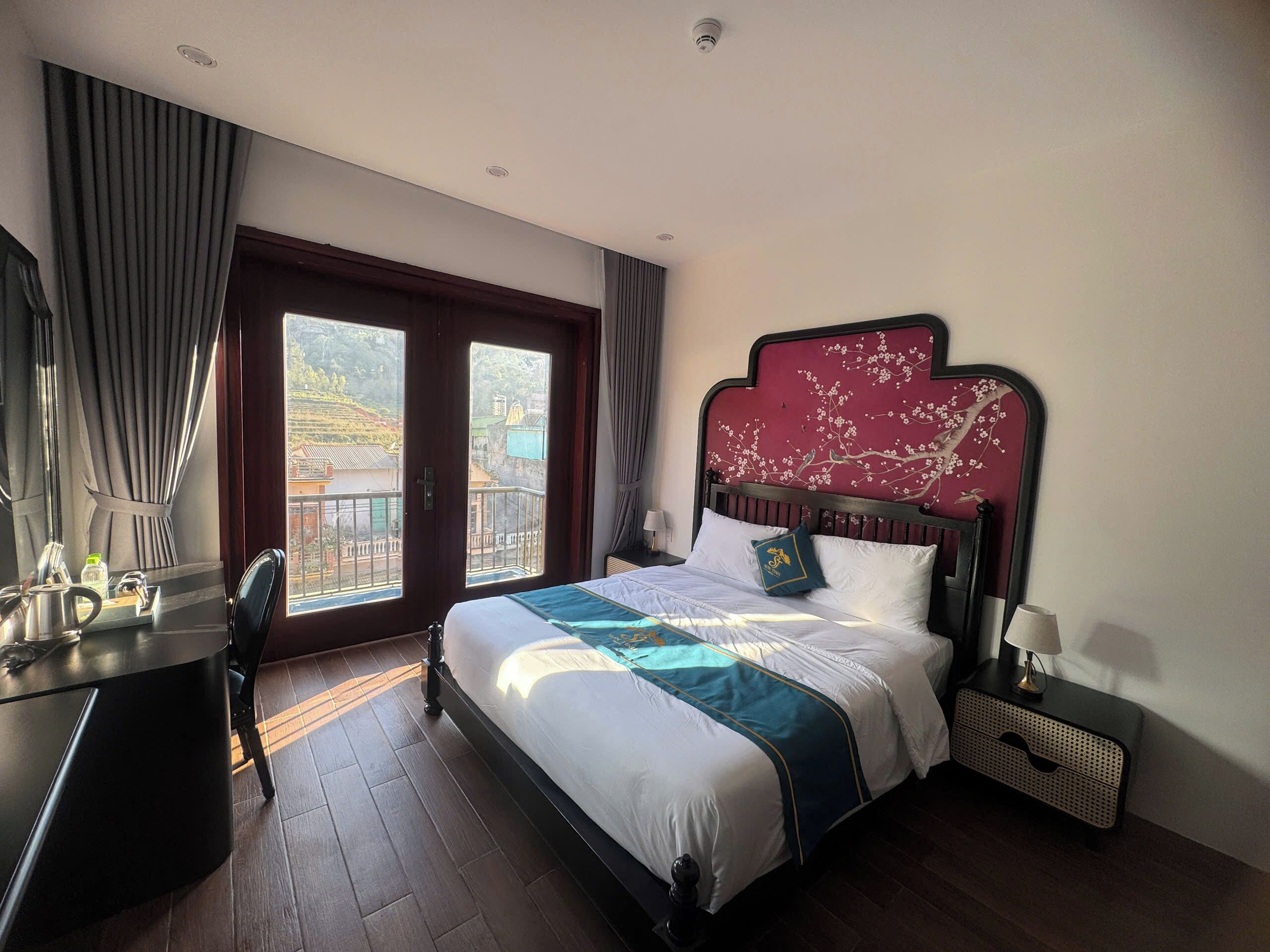 A hotel room with a large bed, a desk, a chair, a nightstand, and a view of the outside.