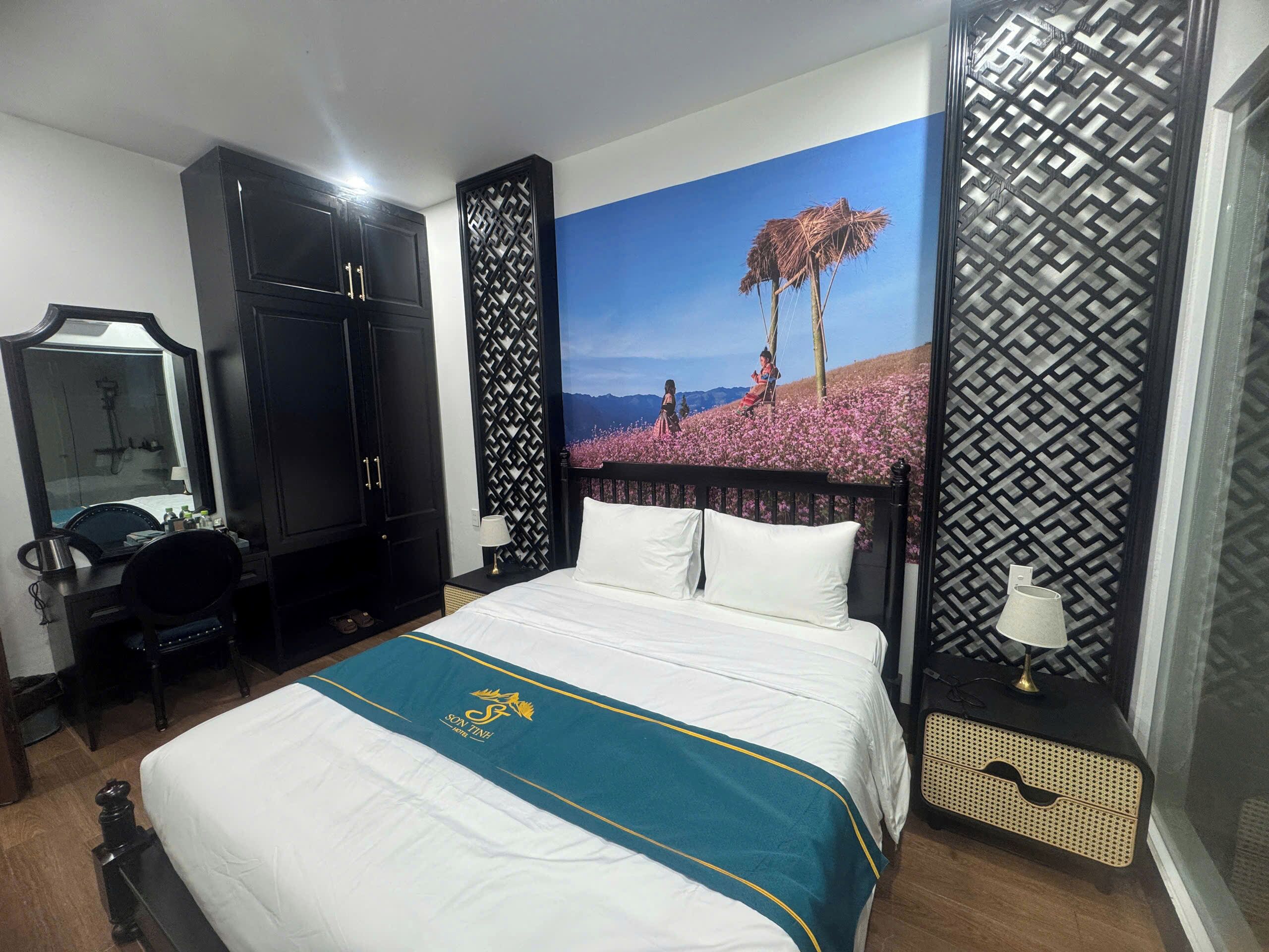 Una camera d'albergo con un letto, una scrivania, una sedia, un armadio e una parete decorata con un dipinto di paesaggio.