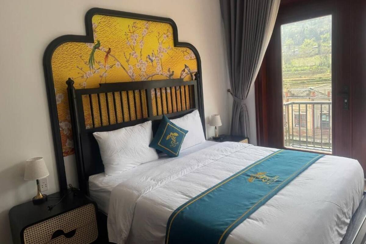 A hotel room with a bed, a nightstand, a lamp, and a view through a window.