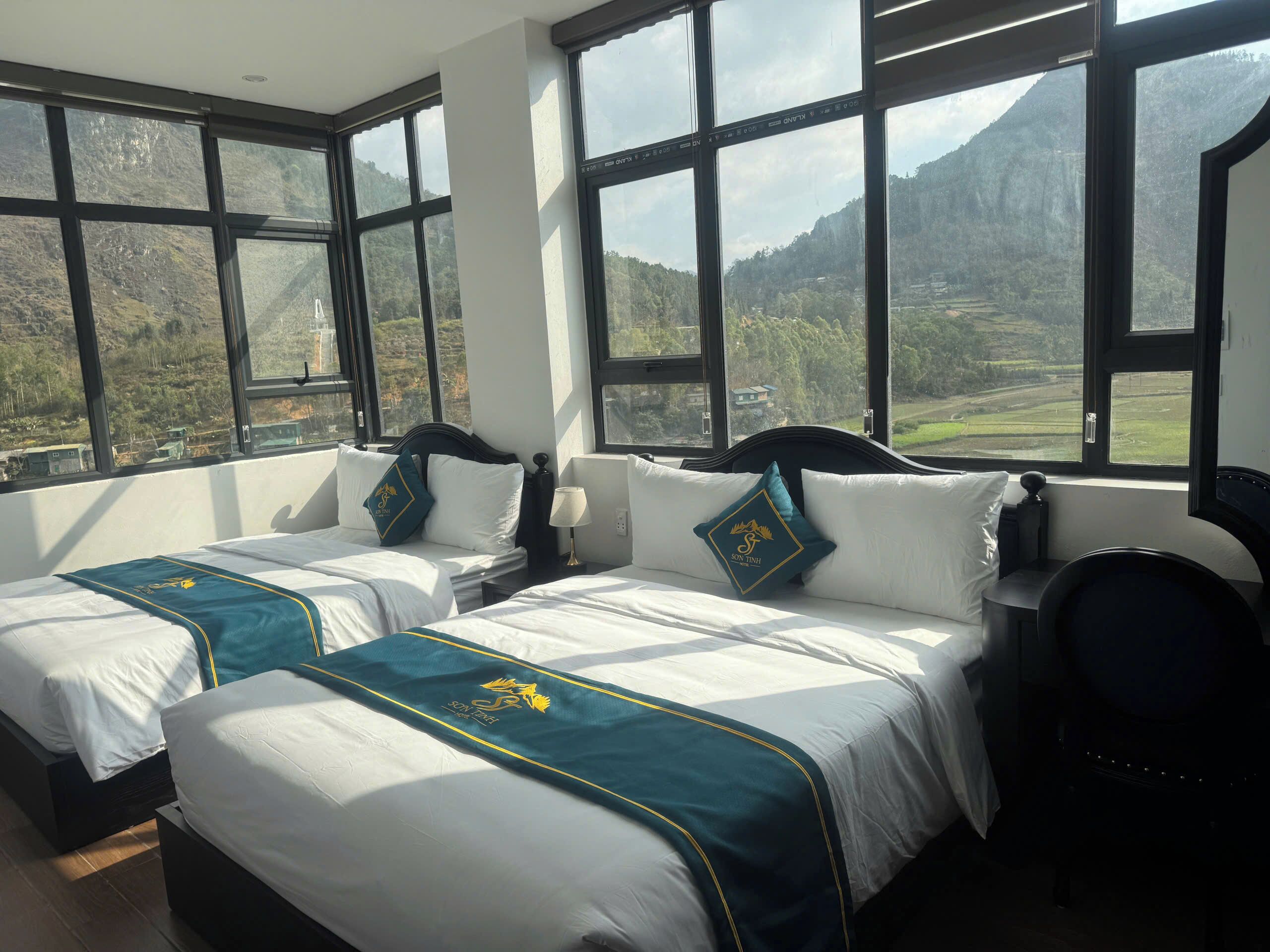 Une chambre d’hôtel avec deux lits, de grandes fenêtres et une vue sur les montagnes.