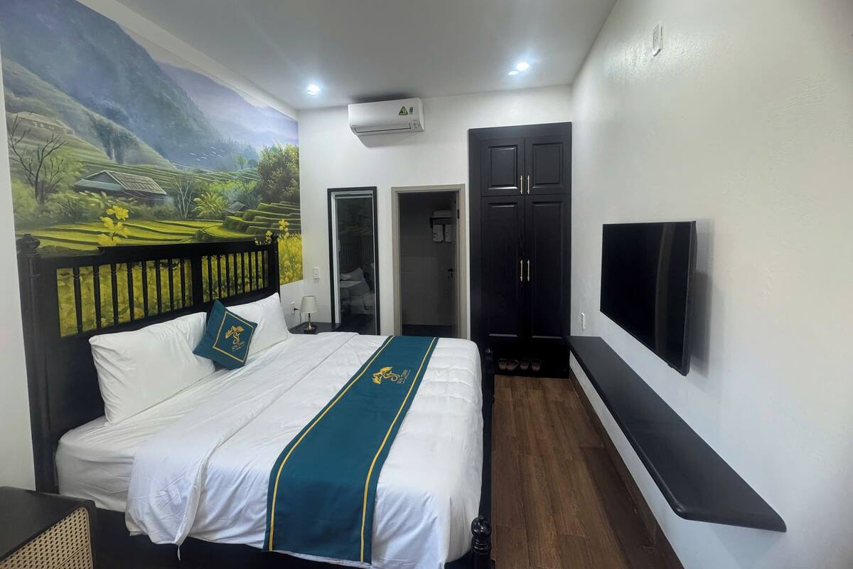 A hotel room with a bed, a TV, a wardrobe, and a mural on the wall.