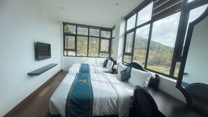 Habitación de hotel con dos camas, un televisor montado en la pared y ventanas amplias con vistas a la montaña.