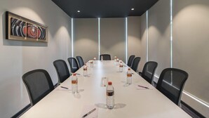 A conference room with a long table, chairs, water bottles, and a painting on the wall.