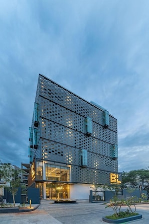 Un edificio moderno con fachada de vidrio, un llamativo letrero 'BL' y un área de entrada ajardinada.