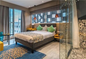 A modern hotel room with a large bed, a desk, and a chair, a glass partition, and patterned walls. - Hotel BL (Hyderabad)