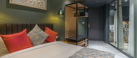 A modern hotel room with a bed, a wooden wardrobe, a walk-in closet, and a bathroom with a glass shower.