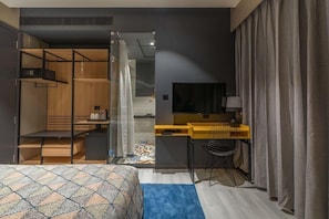 A compact hotel room with a bed, a desk, a TV, and a shower area. - Hotel BL (Hyderabad)