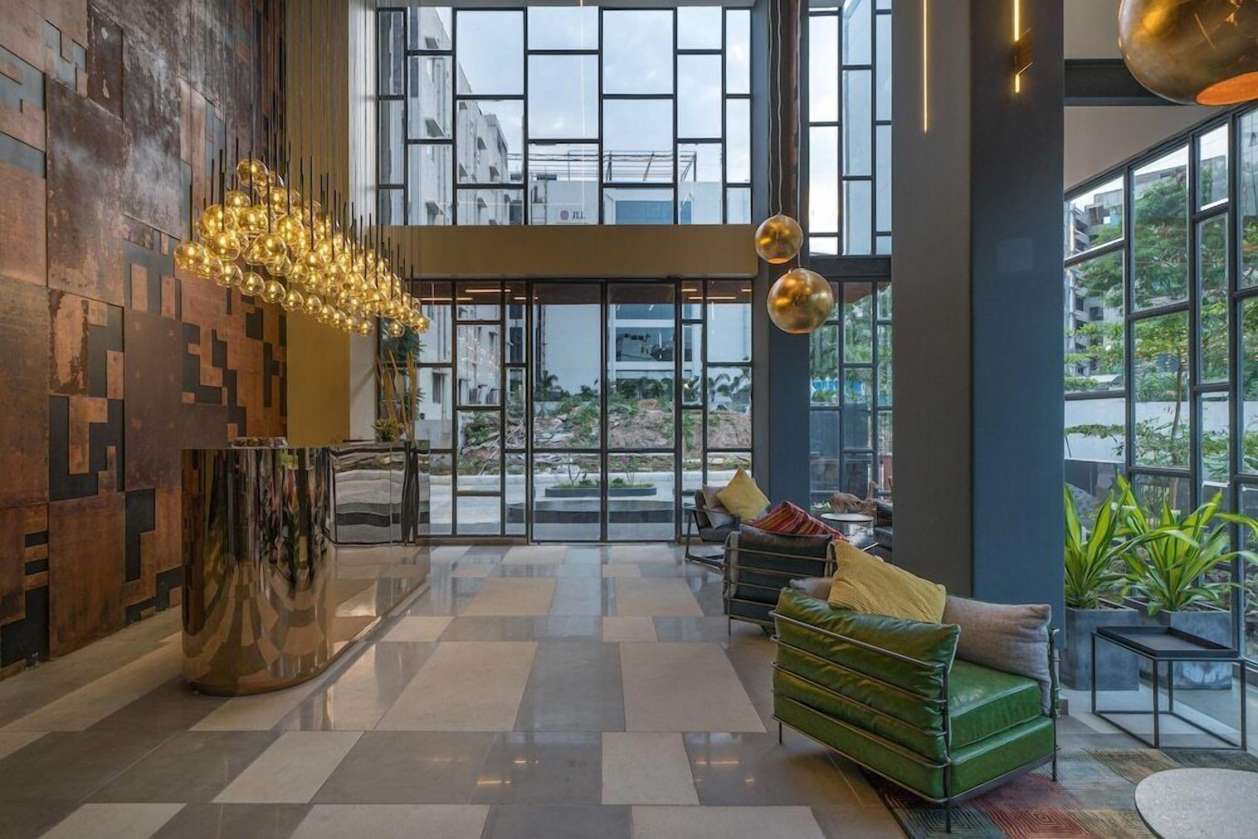 A spacious lobby with a modern chandelier, a green sofa, and large windows offering a view of the city.