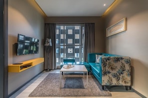 A modern living room with a flat-screen TV, a sofa, a coffee table, and a large window with curtains. - Hotel BL (Hyderabad)