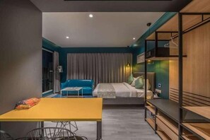 A modern hotel room with a bed, a blue sofa, a dining table, and a wooden shelving unit. - Hotel BL (Hyderabad)