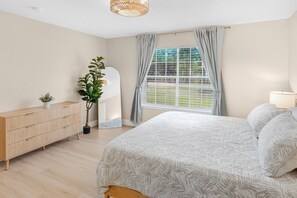 A bedroom with a bed, a dresser, a plant, and a window with curtains. - Casa Palma | Modern Coastal Retreat (Destin)
