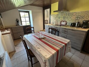 A kitchen with a dining table, chairs, a coffee maker, and a tiled backsplash. - Gîte d'Angouade - SAINT PAUL LES DAX (SAINT PAUL LES DAX)