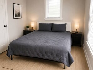 A bedroom with a bed, two bedside tables, a window, and a door. - The Wilson - 67 Side (Columbus)