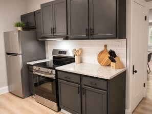 A modern kitchen with dark cabinets, stainless steel appliances, a granite countertop, and a knife block. - The Wilson - 67 Side (Columbus)