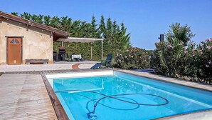 Una piscina con muelle de madera, un espacio de estar techado al aire libre y un edificio con puerta y ventanas.