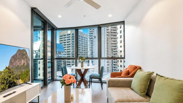 A modern living room with a large window, a ceiling fan, a sofa, and a coffee table. - Resort-Style CBD 1-Bedroom Stay Walk to Everything (Brisbane City)