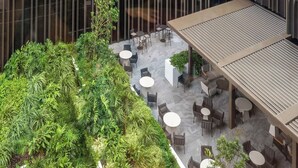 An outdoor seating area with tables and chairs, surrounded by lush greenery and a modern building facade. - Resort-Style CBD 1-Bedroom Stay Walk to Everything (Brisbane City)