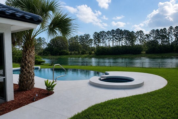 A modern pool with a hot tub, surrounded by a well-maintained lawn and a body of water. - Dreamin O'Sprey! Amazing View & Plenty O'Privacy! (Clermont)