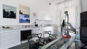A modern kitchen with white cabinetry, a glass dining table, and decorative items. - Terrazza Di Sorrento, Town Centre Apartment (Sorrento)