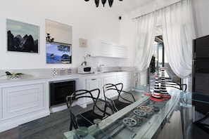 A modern kitchen with white cabinetry, a glass dining table, and decorative items. - Terrazza Di Sorrento, Town Centre Apartment (Sorrento)