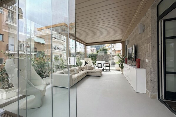 A modern living room with a sectional sofa, a glass partition, and a view of the cityscape. - Terrazza Di Sorrento, Town Centre Apartment (Sorrento)